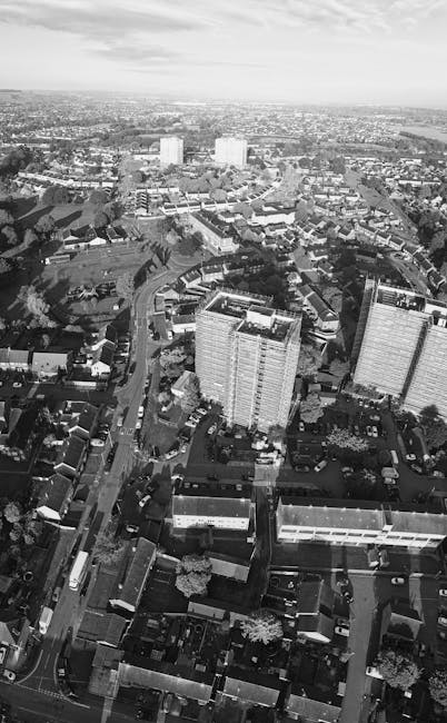 An aerial view of the town centre in Harefield, showing a mixture of residential and commercial buildings with a variety of rooftops, parked cars along the streets, and a body of water on the right si