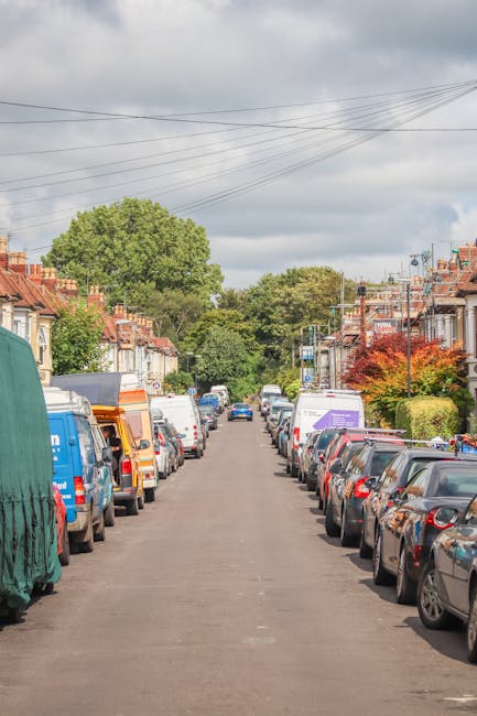 A residential street scene in Harefield during daytime, featuring a row of traditional red brick terraced houses with white window frames and pitched roofs, some with bay windows and small front garde